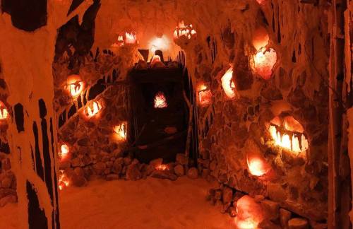 A dimly lit room with stone walls, illuminated by glowing salt lamps and covered in salt crystals.