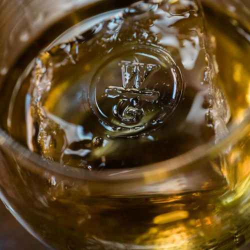 Close-up of a glass with whiskey and a large ice cube featuring a logo, creating a rich, amber-colored drink.