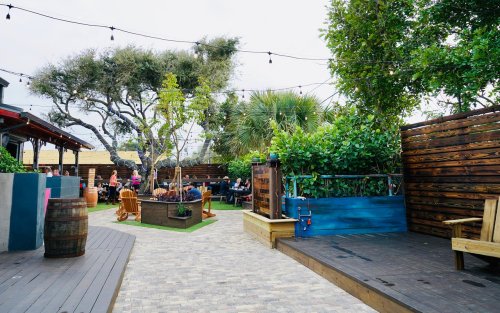 Outdoor dining area with wooden seating, greenery, and string lights, creating a cozy atmosphere.