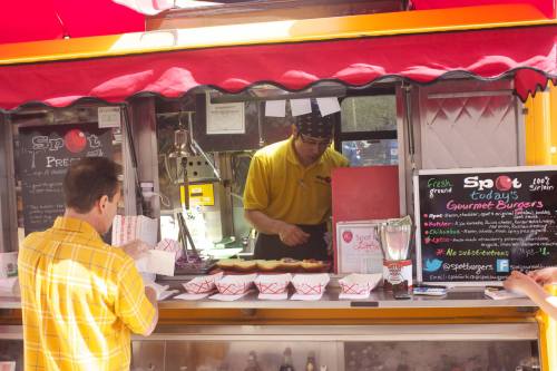 A food truck serving gourmet burgers, with a chef in a yellow shirt and a customer ordering at the counter.