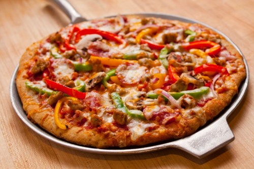 A freshly baked pizza topped with colorful bell peppers, onions, mushrooms, and sausage on a metal serving tray.