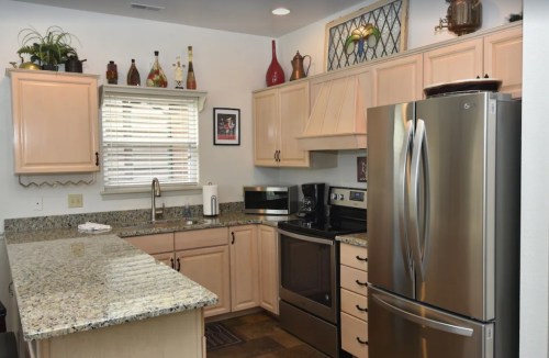 A modern kitchen with light wood cabinets, granite countertops, stainless steel appliances, and a window with natural light.