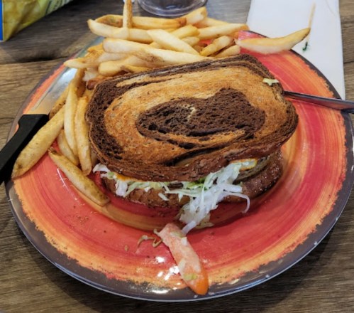 A plate with a sandwich made of dark bread, filled with lettuce and a patty, accompanied by a side of fries.