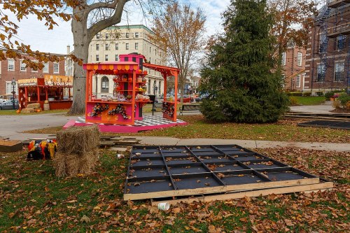 A colorful vendor stand with decorations sits in a park, surrounded by fallen leaves and wooden platforms.