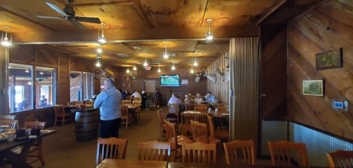 Interior of a rustic restaurant with wooden decor, tables, and a TV showing a sports game. Patrons are dining.