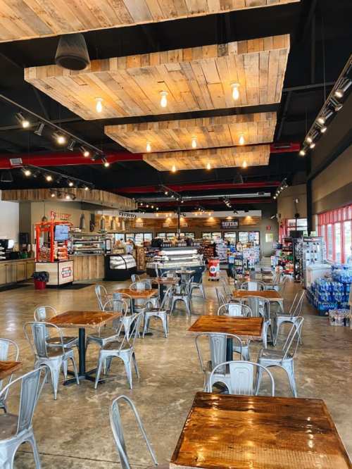 A spacious café interior with wooden beams, metal tables, and a display counter filled with food and drinks.