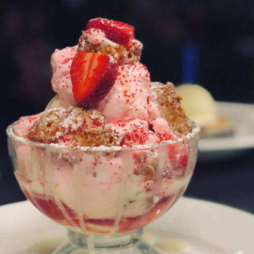 A delicious dessert in a glass, featuring pink ice cream, strawberries, and sprinkles, topped with whipped cream.