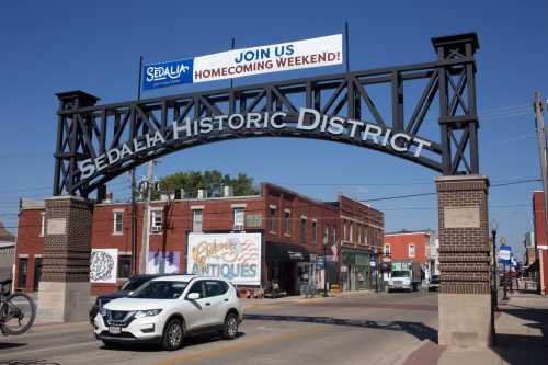 Archway sign for Sedalia Historic District with a banner promoting Homecoming Weekend, cars passing below.