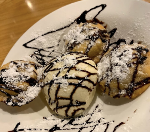 Four dessert balls drizzled with chocolate sauce and dusted with powdered sugar on a white plate.