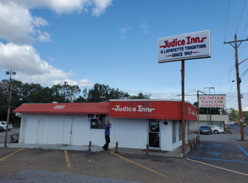 A small restaurant with a red roof and sign reading "Judice Inn" in Lafayette, Louisiana, with a person walking by.