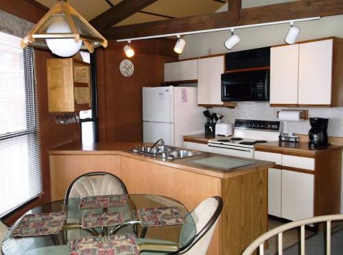 A modern kitchen with wooden cabinets, a dining table, and appliances like a refrigerator, microwave, and coffee maker.