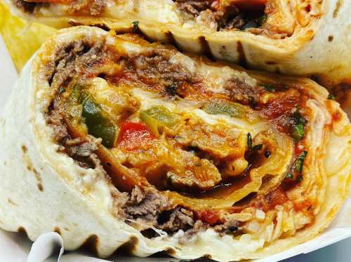 Close-up of a sliced burrito filled with beef, cheese, and colorful vegetables wrapped in a tortilla.