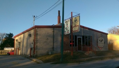 A corner building with a red roof and signage, featuring a large window and a chimney, set against a clear sky.