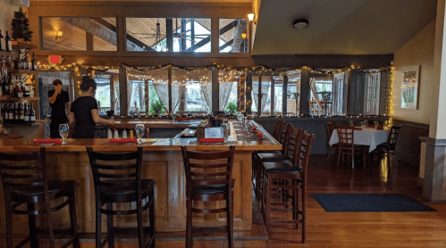 Cozy restaurant interior with a wooden bar, tables, and string lights, creating a warm ambiance.