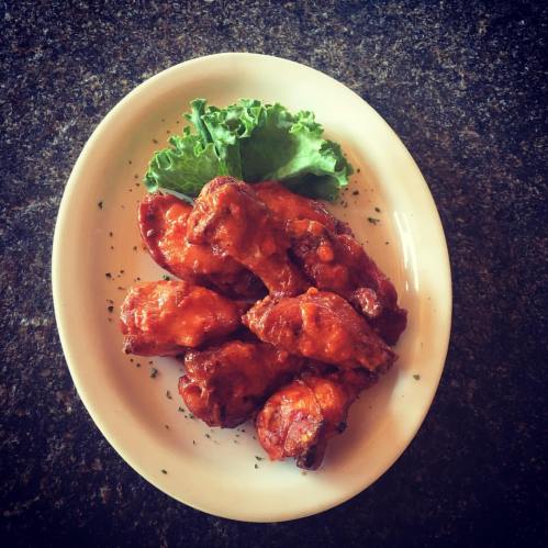 A plate of saucy chicken wings garnished with lettuce on a dark countertop.