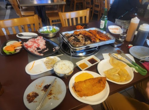 A table filled with various dishes, including grilled meats, rice, sauces, and side dishes, in a casual dining setting.