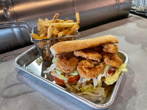 A plate with a shrimp sandwich on a hoagie roll, lettuce, and tomato, alongside a basket of golden fries.