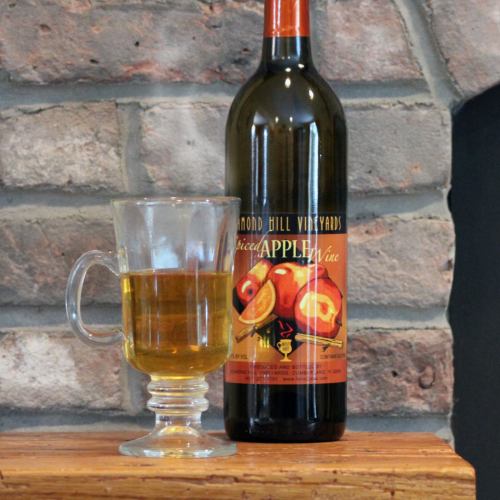 A bottle of spiced apple wine next to a glass filled with the wine, set against a stone wall background.