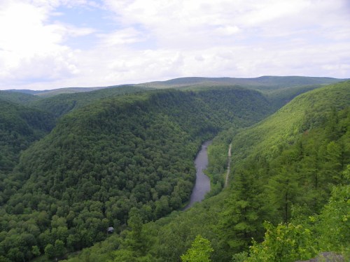 A lush green valley with rolling hills and a winding river, under a partly cloudy sky.