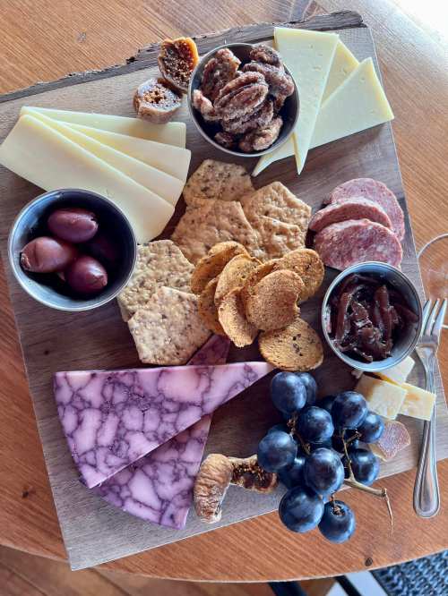 A wooden platter with assorted cheeses, crackers, olives, nuts, salami, figs, and grapes arranged artfully.