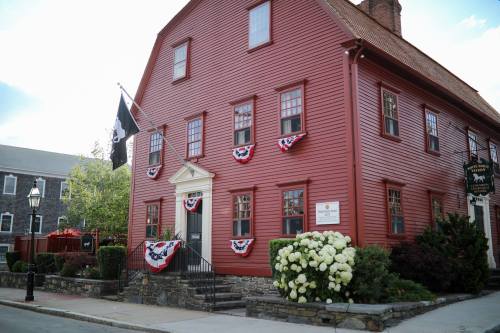 A red historic building adorned with patriotic bunting and surrounded by greenery and flowers.