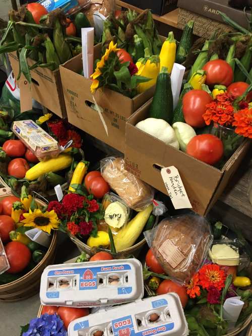 Boxes filled with fresh vegetables, flowers, and eggs, arranged in a market setting.