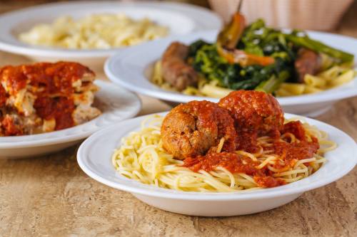 A plate of spaghetti topped with meatballs and marinara sauce, with other pasta dishes in the background.