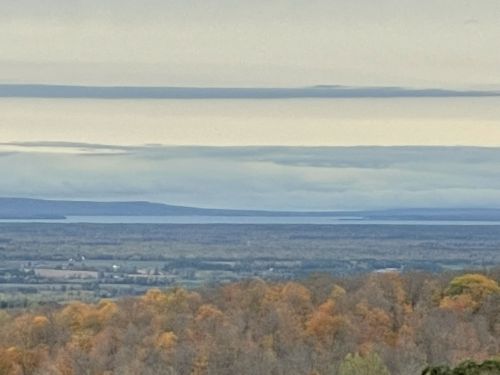 A panoramic view of a landscape with rolling hills, a lake in the distance, and a cloudy sky above.