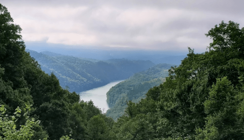 A scenic view of a winding river surrounded by lush green mountains under a cloudy sky.