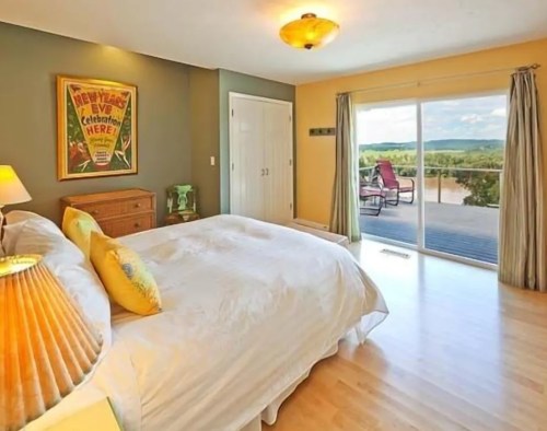 Bright bedroom with a large bed, colorful decor, and a view of a deck overlooking scenic hills.