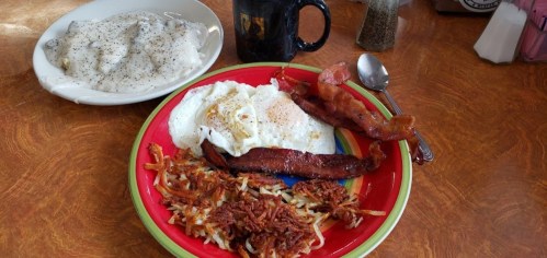 A colorful plate with eggs, bacon, hash browns, and a side of gravy-covered biscuits on a wooden table.
