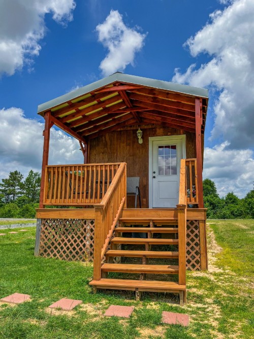A small wooden cabin with a porch and steps, set against a blue sky with fluffy clouds and green grass.