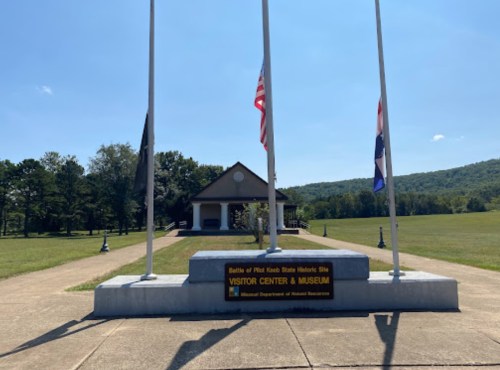 Visitor center and museum at the Battle of Pilot Knob State Historic Site, with flags and a clear blue sky.
