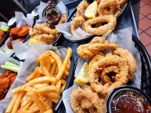 Two baskets of fried calamari with lemon wedges and dipping sauce, accompanied by a side of golden French fries.