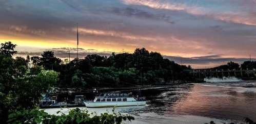 A serene river scene at sunset, with a boat docked and colorful clouds reflecting in the water.