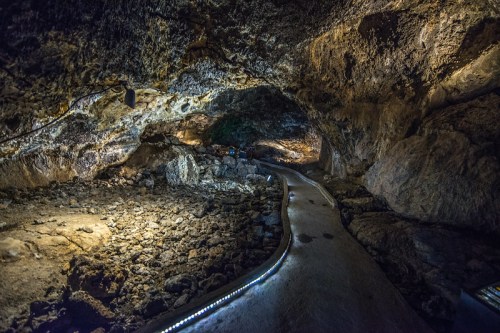 A dimly lit cave interior with a rocky floor and a winding pathway illuminated by soft lights.