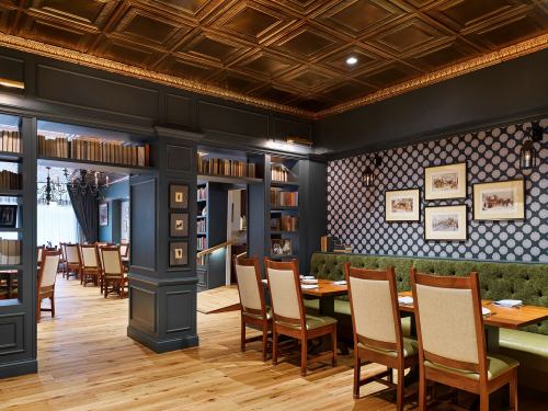 Elegant restaurant interior featuring wooden floors, green upholstered seating, and decorative bookshelves.