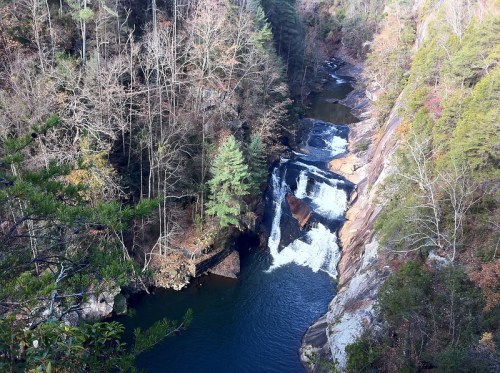 A scenic view of a waterfall cascading into a serene river, surrounded by trees and rocky cliffs.