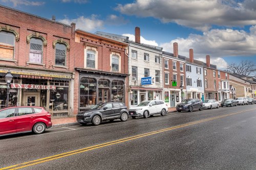 A charming street lined with historic brick buildings and parked cars under a cloudy sky.