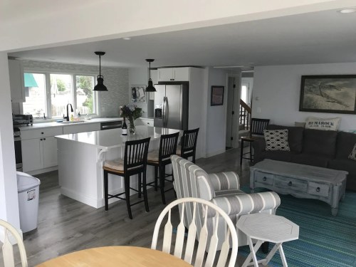Bright, modern kitchen and living area with white cabinets, a gray sofa, and a dining table in a cozy, open layout.