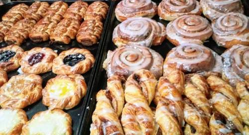 A variety of baked pastries, including cinnamon rolls and fruit-filled danishes, arranged on a tray.