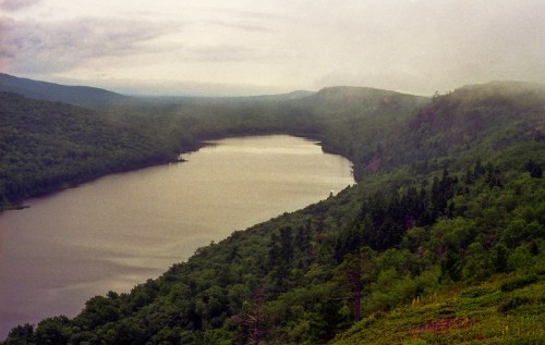 A misty landscape featuring a winding river surrounded by lush green forests and distant mountains.