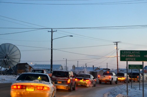 Traffic on a snowy road near a sign for the Legislative Information Office, with a satellite dish in the background.