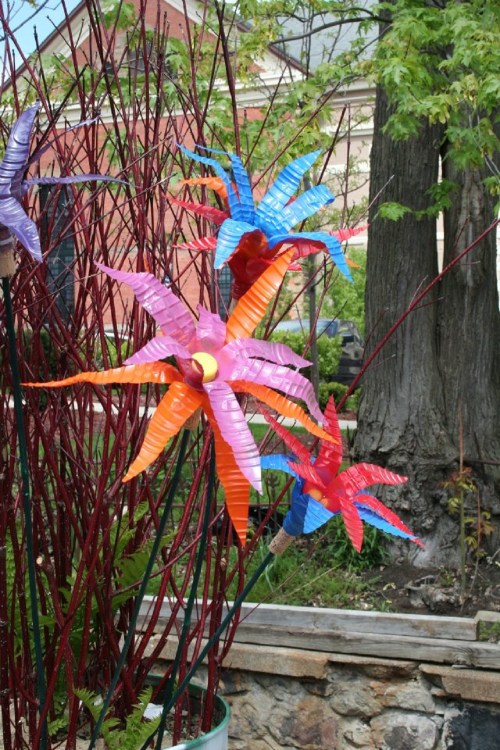 Colorful plastic flowers in vibrant shades of pink, blue, and orange, set against a backdrop of greenery and trees.