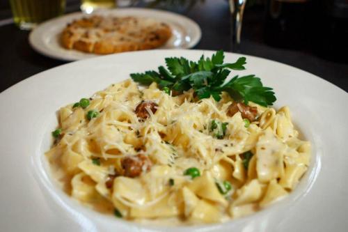 A plate of creamy pasta with peas and herbs, garnished with parsley, alongside a cookie on a table.