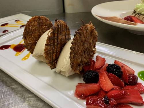 A dessert plate featuring three scoops of ice cream with crispy wafers and a mix of fresh berries on the side.