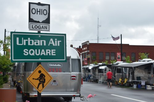 Sign for Urban Air Square in Logan, Ohio, with Airstream trailers and a guitar-playing figure warning sign.