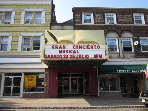 Marquee of a theater announcing a musical concert on July 23 at 8 PM, with nearby storefronts visible.