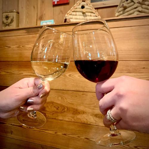 Two hands clink wine glasses, one filled with white wine and the other with red, against a wooden backdrop.