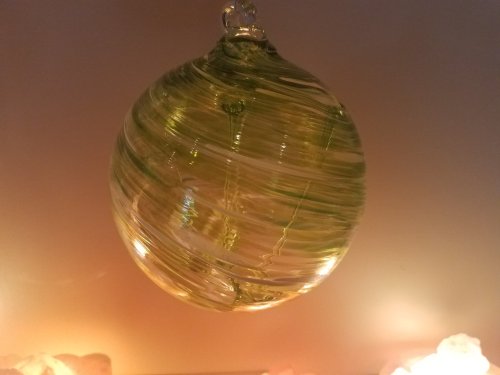 A green glass ornament with swirling patterns, suspended against a softly lit background.